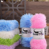 A collection of fluffy faux fur yarn in blue, white, green, and pink colors displayed on a wooden surface.