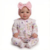 A realistic 18-inch reborn baby doll with a pink bow and floral print clothing.