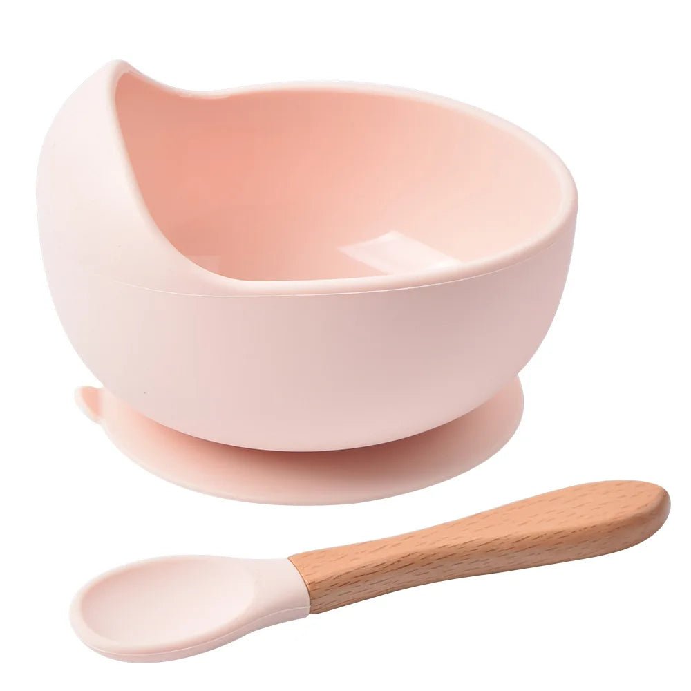 A pink BPA-free silicone snack cup with a lid is shown next to a wooden spoon.