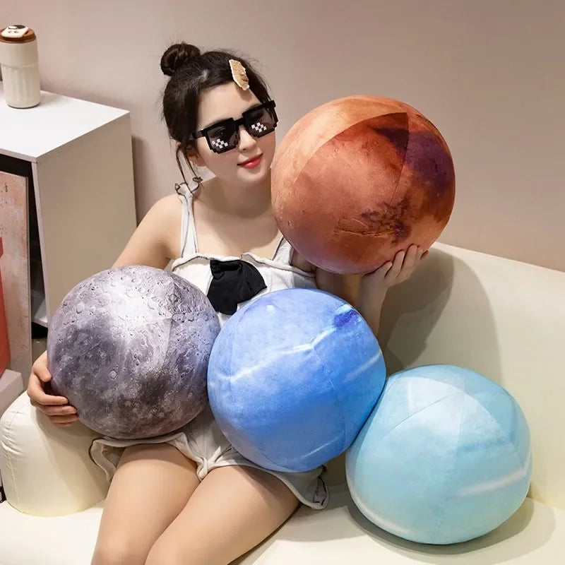 A young woman is sitting with several spherical plush toys in shades of orange, purple, and blue.