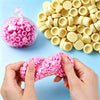 A hand is holding pink plastic beads, with a large pile of yellow bead filler in the background.
