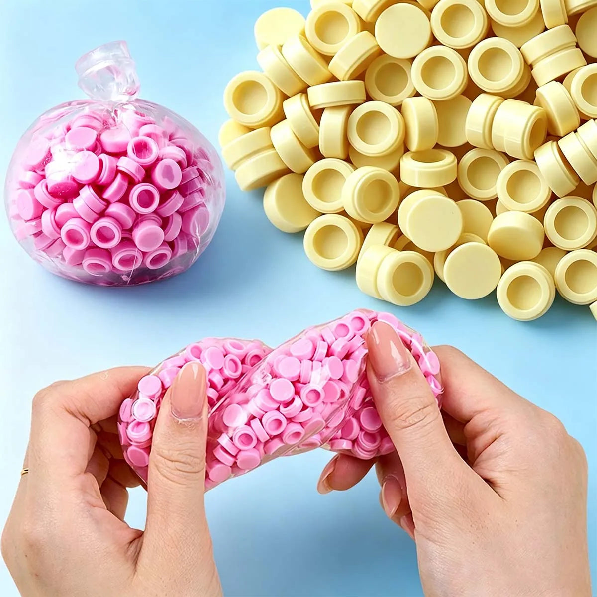 A hand is holding pink plastic beads, with a large pile of yellow bead filler in the background.