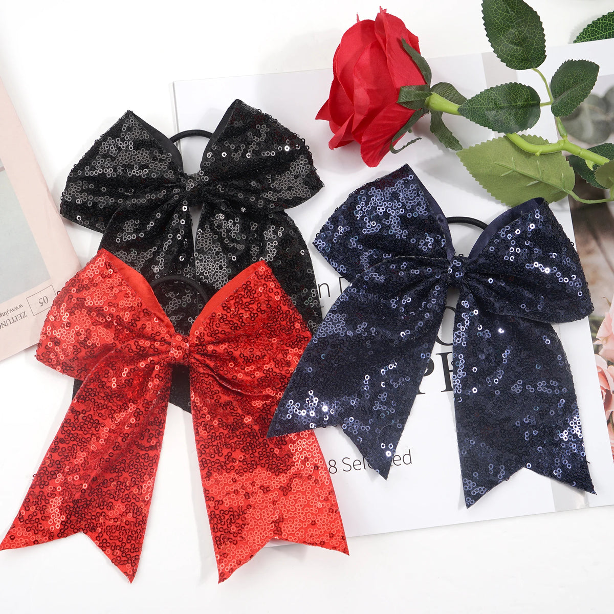 A set of three glitter sequin pigtail bows in black, red, and navy blue are displayed on a white surface.