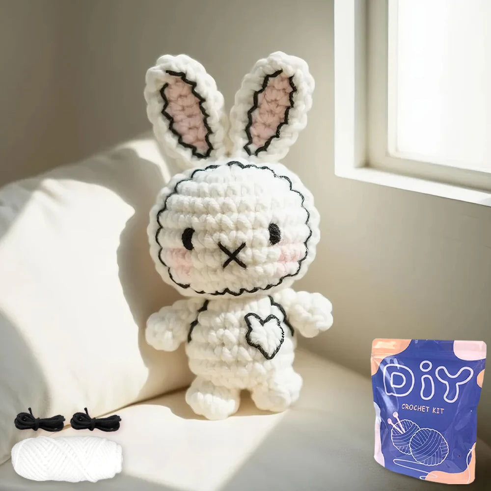 Un lapin tricoté blanc avec des accents roses, assis sur un coussin de canapé clair.