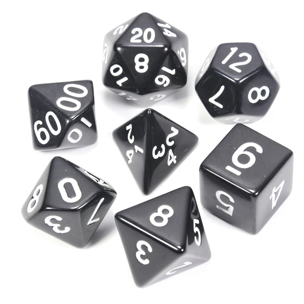 A collection of black acrylic dice, including a d20, d12, and various polyhedral dice, scattered on a white surface.