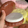 A hand holds a realistic cake squishy fidget toy in various colors including pink, orange, and yellow.