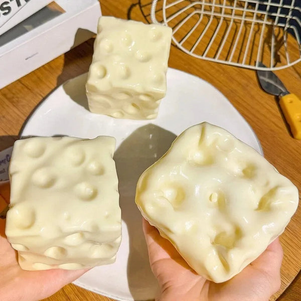 A hand holds a white moldable squishy fidget toy on a plate with other squishies in the background.