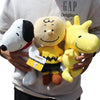 A person holds a yellow Peanuts Snoopy plush toy against a white background.