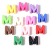 A collection of colorful acrylic letter M beads in various shades including yellow, pink, purple, blue, green, and red.