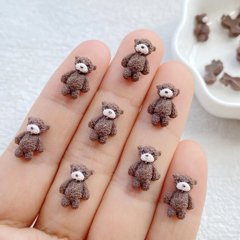 A hand displays several small, dark brown resin teddy bear charms for DIY crafts.