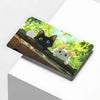 A cute black cat peering over a wooden ledge with green foliage in the background.