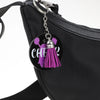A black pouch with a silver charm featuring purple velvet tassels and the word cheer