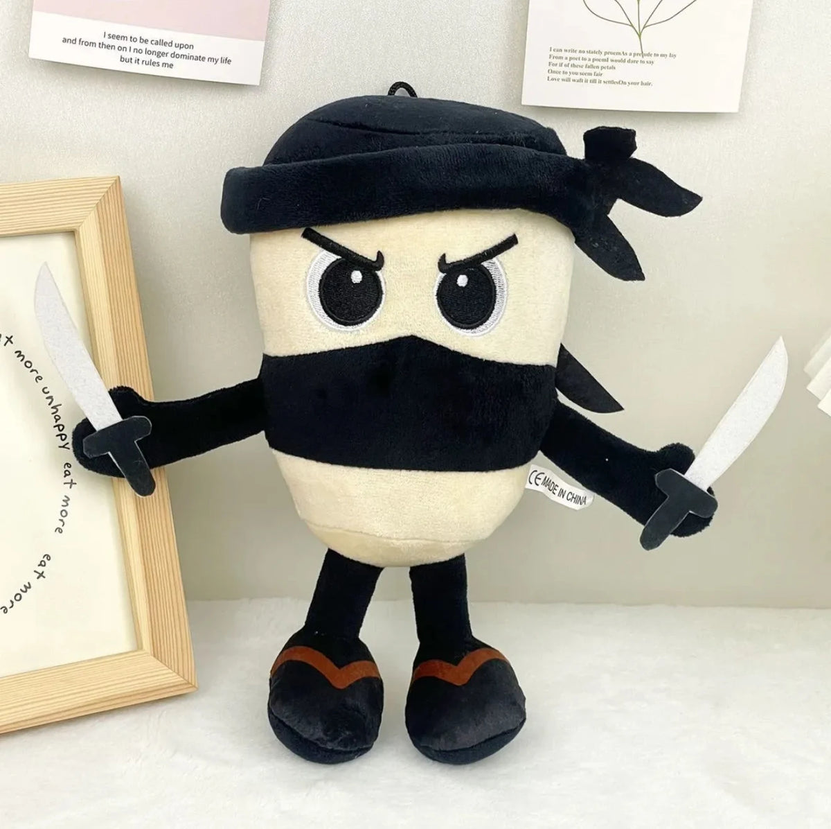A black and tan plush toy resembling a shark with a hood and small swords.