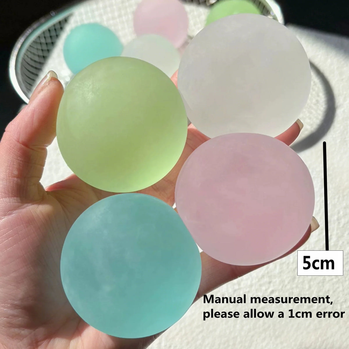 A hand holds several round, pastel-colored squishy toys, including light green, pink, and blue shades.