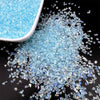 A pile of crushed light blue crystal glass mix for resin and jewelry making next to a white container.