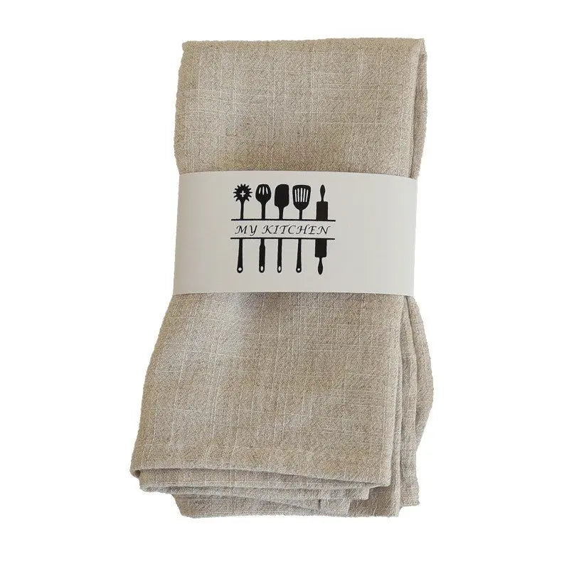 A stack of beige cotton-linen dinner napkins with a white label featuring kitchen utensils.