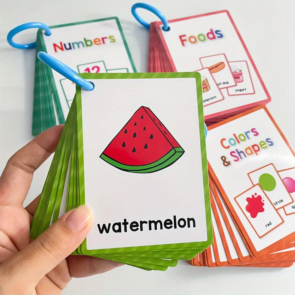 Une main tient une carte verte avec une illustration de pastèque, à côté d'autres cartes d'apprentissage pour les nombres, le