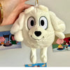 A white plush dog toy resembling a puppy is being held by a hand against a background of children's illustrations.