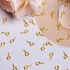 A collection of gold-colored metal eye pins scattered on a white surface next to a beige hat.