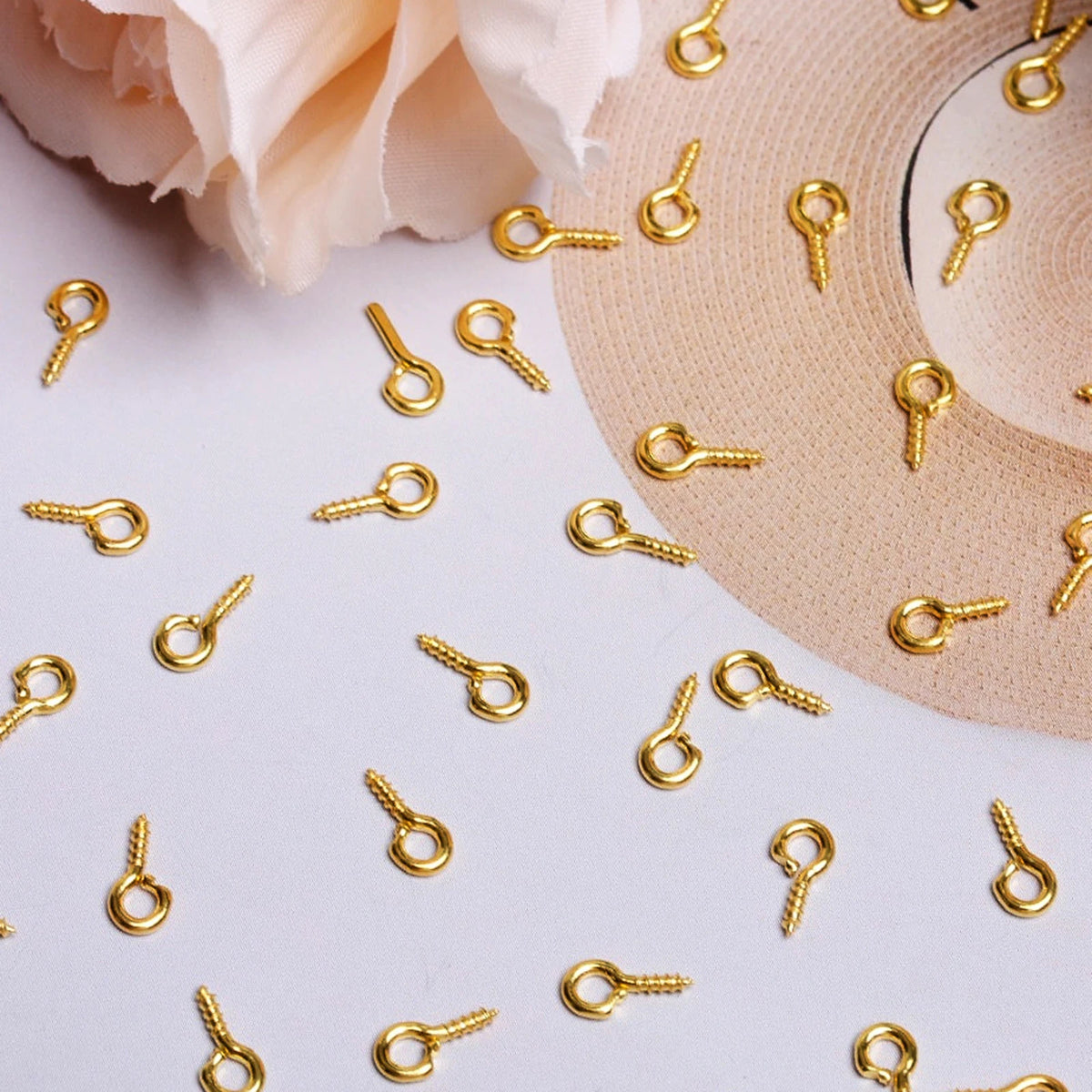 A collection of gold-colored metal eye pins scattered on a white surface next to a beige hat.