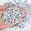 A hand holds a pile of silver sparkling crystal flatback rhinestones for nail art and crafts.