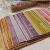 A close-up of a stack of rainbow textured paper sheets in various shades and stripes.