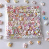 A clear plastic container filled with pink and purple floral squishy stress relief fidget toys scattered on a white surface.