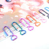 A set of heart-shaped diamond painting canvas clips in various colors are displayed on a patterned grid.