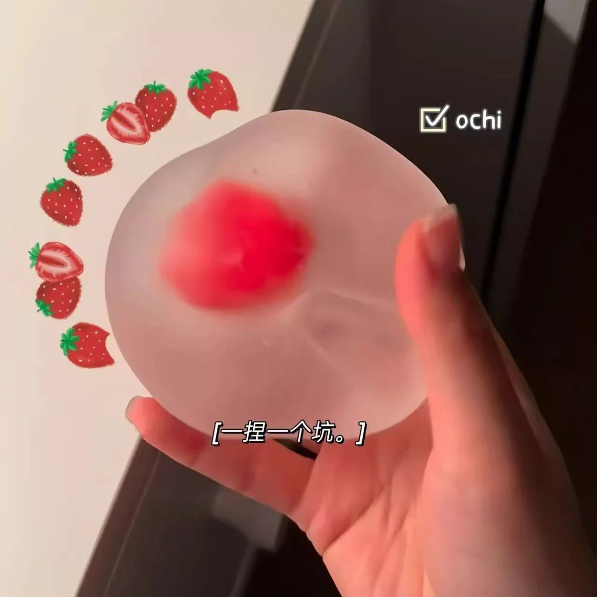 A hand holds a pink mochi squishy stress relief toy with a red center, demonstrating its texture.
