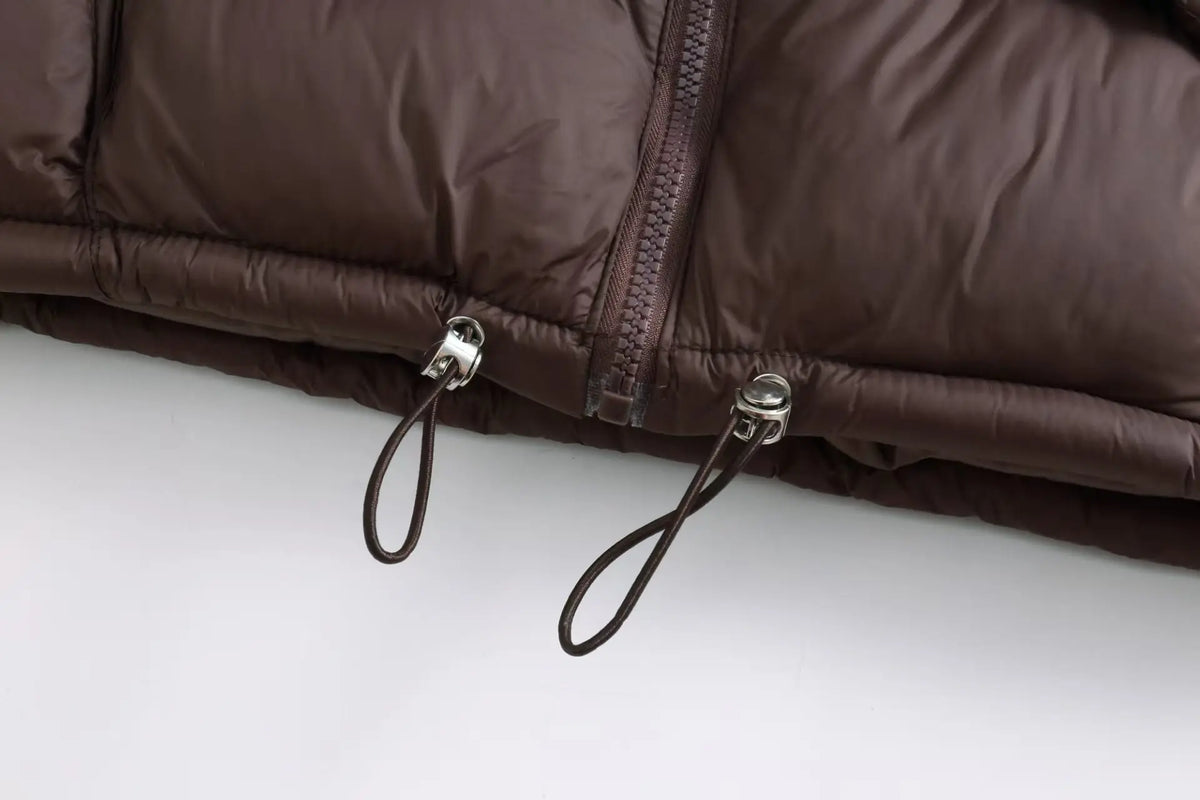 Close-up of a dark brown padded down vest with silver zippers and leather drawstrings.