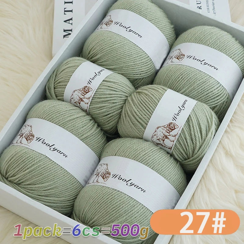 A box containing six balls of light green merino wool yarn with brown labels and a product number tag.