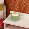 A miniature light green copper soup pot with a gold lid displayed on a white shelf.