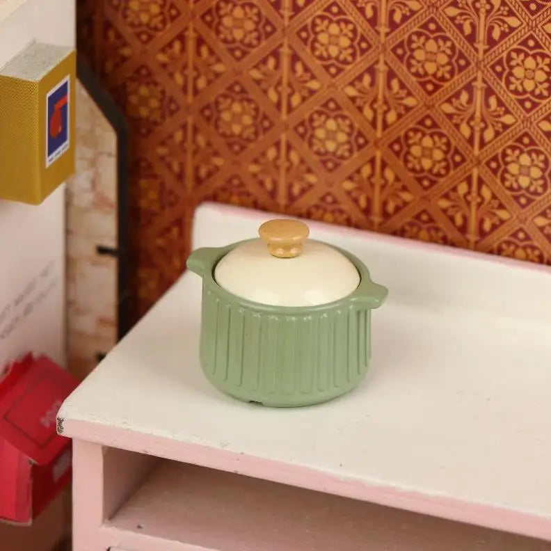 A miniature light green copper soup pot with a gold lid displayed on a white shelf.
