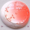 A round, translucent pink liquid slime is displayed in a white dish on a gray fabric background.
