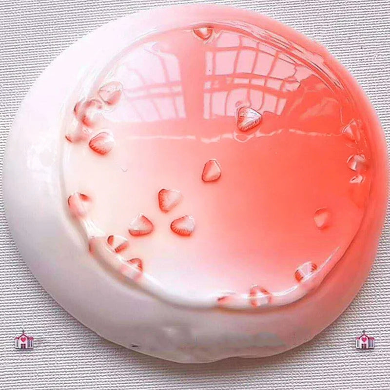 A round, translucent pink liquid slime is displayed in a white dish on a gray fabric background.