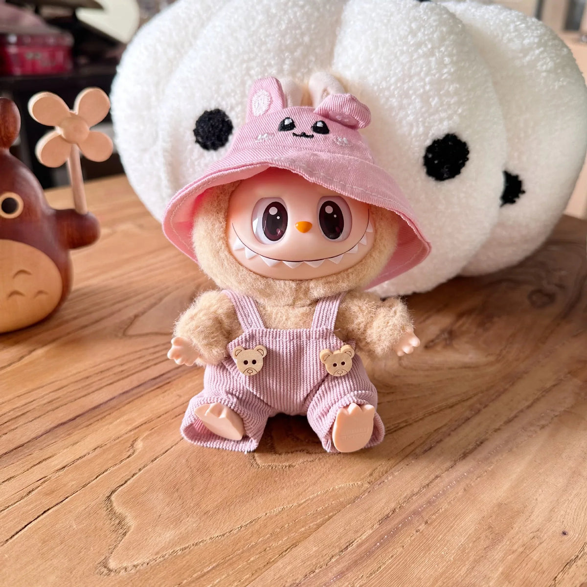 A Labubu doll wearing a pink hooded outfit and a white fuzzy hat with black polka dots.