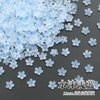 A pile of light blue sakura flower crystal glass beads scattered on a dark surface.