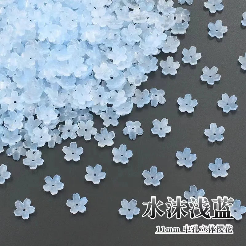A pile of light blue sakura flower crystal glass beads scattered on a dark surface.
