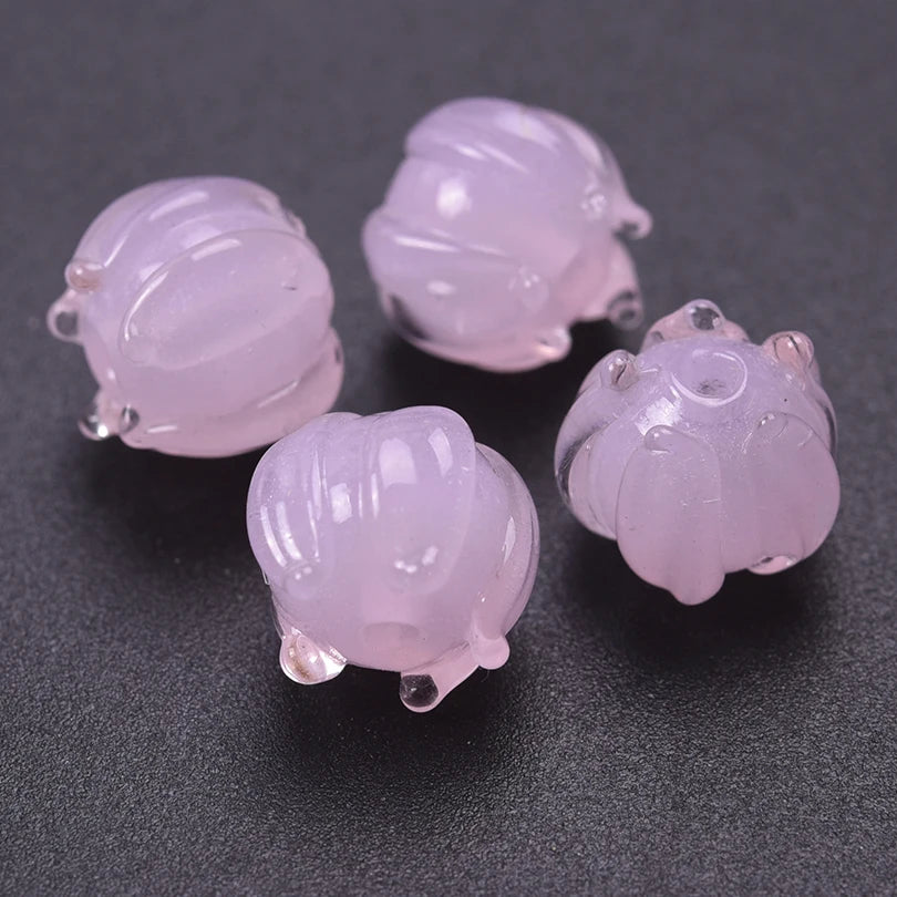 Several translucent pink glass charm pendants shaped like lily of the valley buds are displayed on a dark surface.