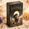 A black box of the Embrace the Fullness Tarot deck resting on a textured surface with dried flowers and crystals.