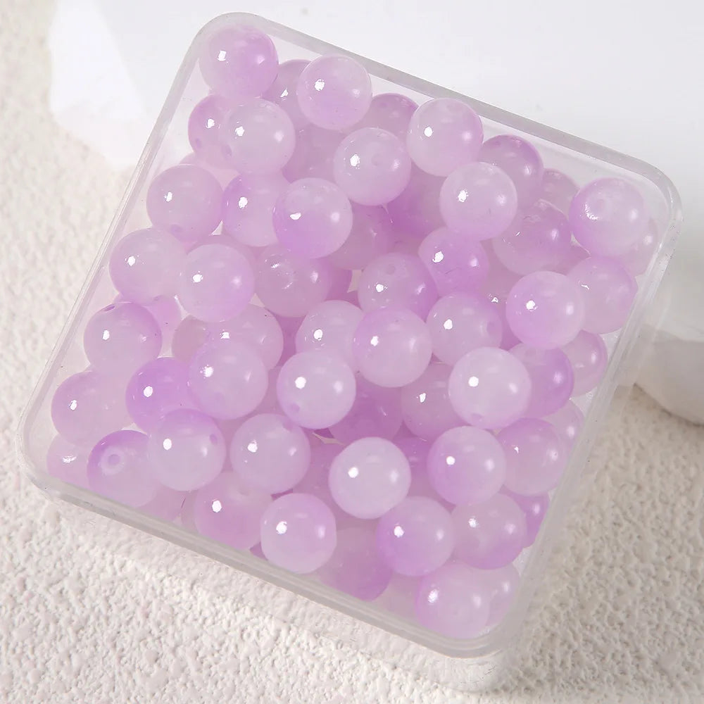 A clear plastic container filled with purple imitation jade glass beads for jewelry making