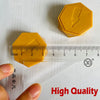 A yellow magnetic strategy board game piece shaped like a hexagon, shown next to a ruler and a hand.