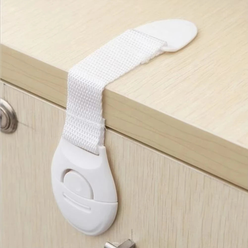A white child safety cabinet lock set featuring a strap and a plastic lock mechanism mounted on a light wood cabinet.