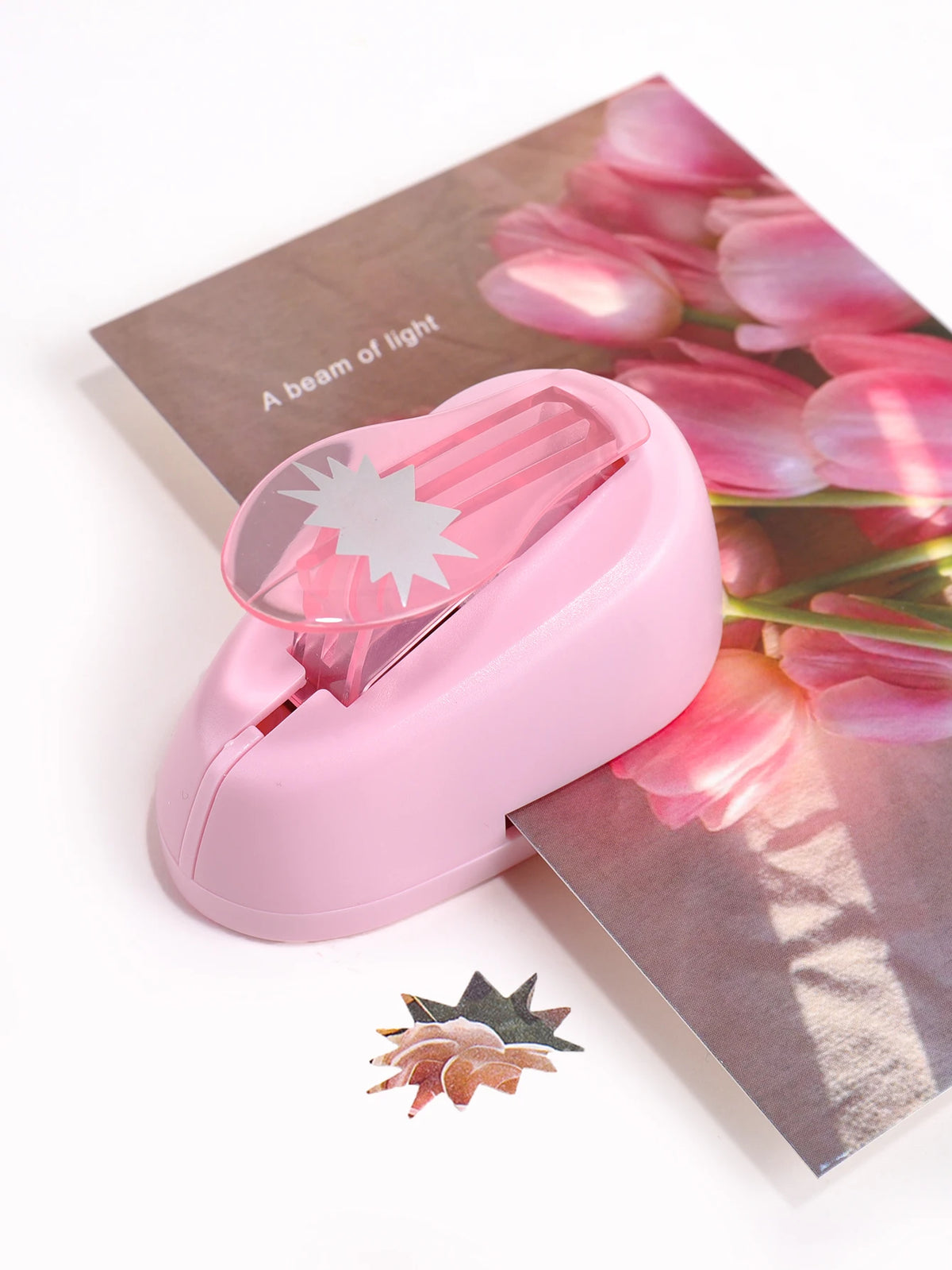A pink lever action embosser tool rests on a sheet of paper with pink tulips.