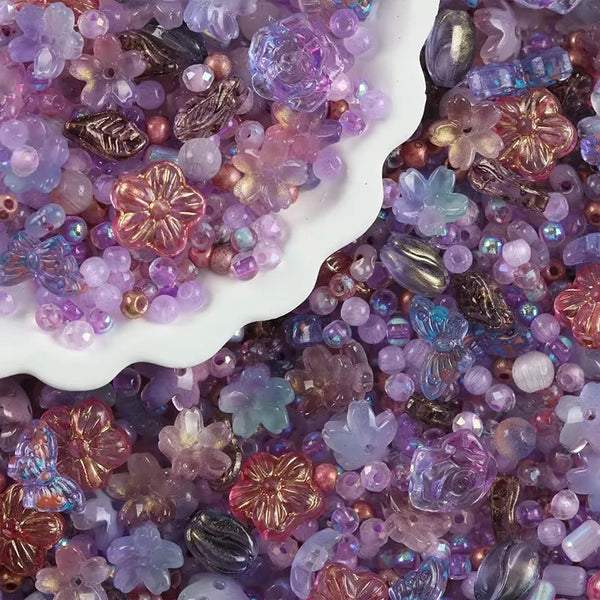 Gros plan de perles en verre violettes et roses mélangées éparpillées sur une surface blanche.