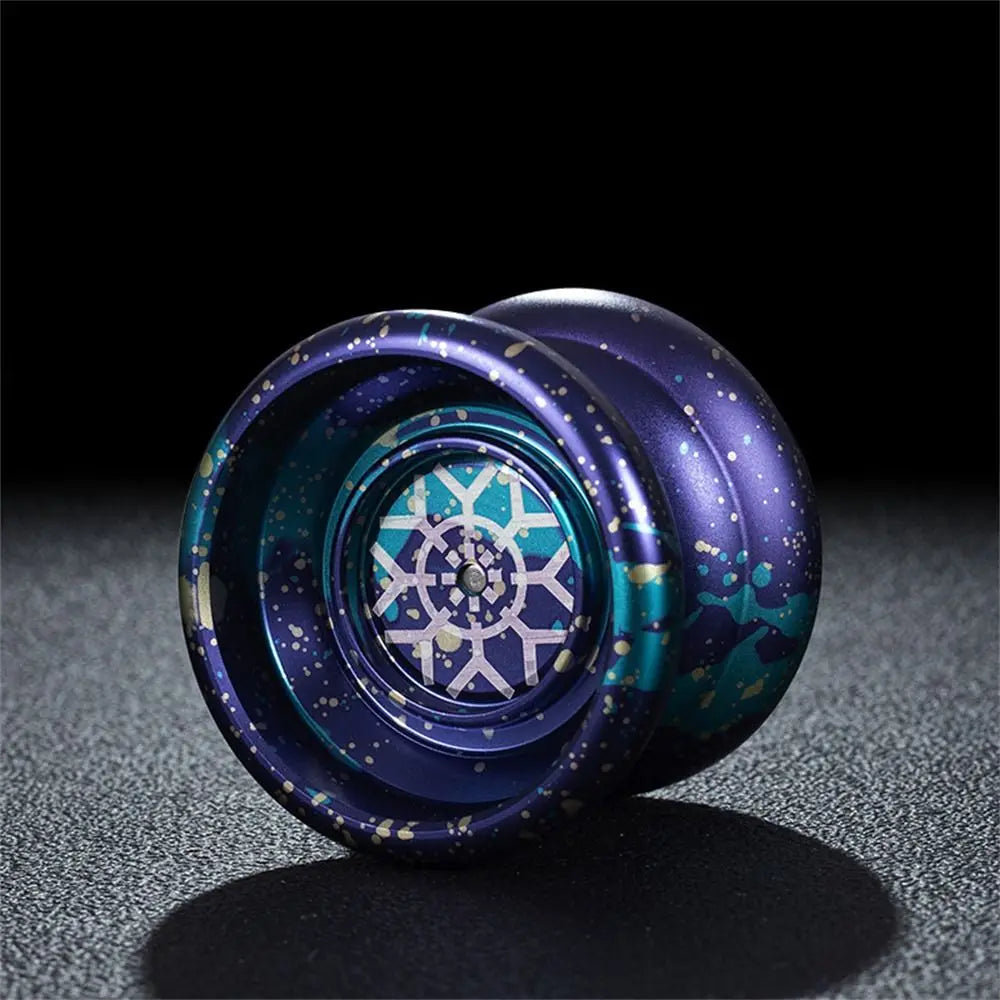 Gros plan d'un yoyo bleu foncé avec des motifs argentés et turquoise, posé sur une surface sombre.
