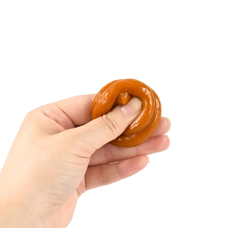 A hand is holding a realistic, soft fake poop toy, which is orange and brown in color.