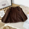 A brown fuzzy lamb wool vest laid flat on a white surface next to a framed picture and natural fibers.