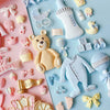 A collection of pink and yellow silicone baby-themed cake molds including a teddy bear, bottle, pacifier, and stroller.
