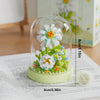 A clear glass dome displays a miniature flower bouquet made of white and yellow building blocks.